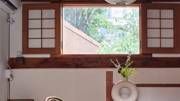 A dining area with a round wooden table, two chairs, a vase with flowers, and a window with a view of greenery.