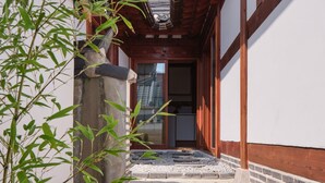 Un bâtiment traditionnel japonais, avec une façade en bois, des marches en pierre menant à une porte et un plant de bambou au premier plan.