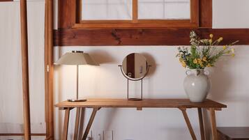 A wooden desk with a lamp, a vase with flowers, and a mirror.
