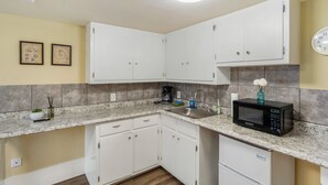 A compact kitchen with white cabinets, a granite countertop, a microwave, and a small refrigerator.