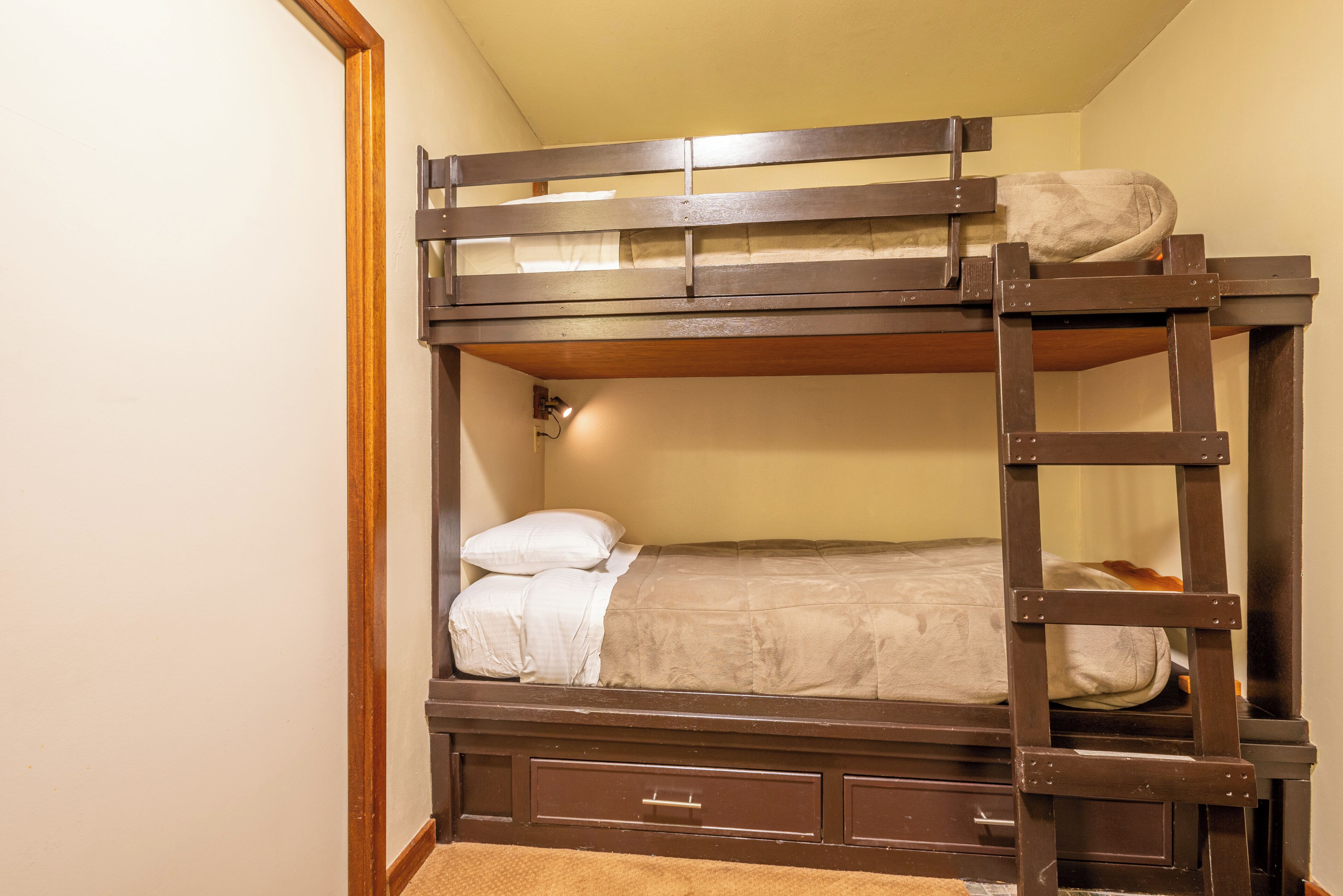 A bunk bed with a ladder, a small drawer, and a bedside lamp.