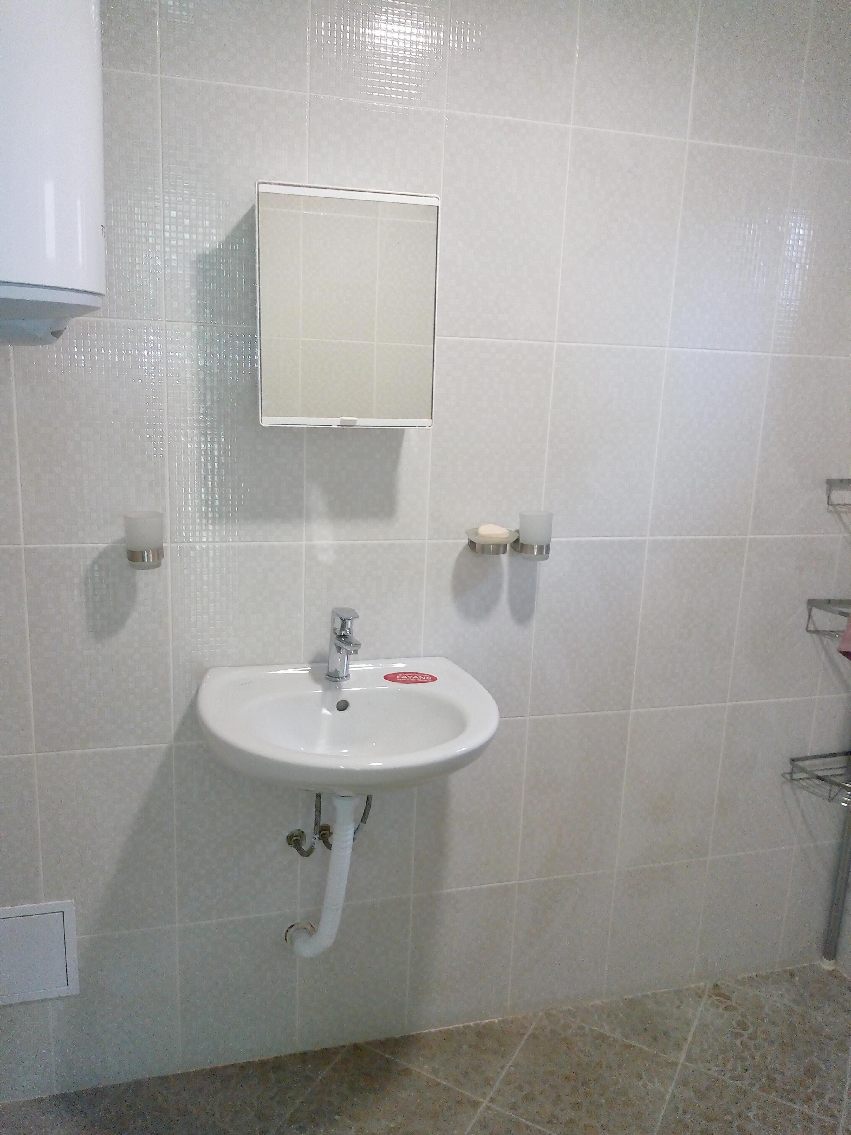 A bathroom with a white sink, a mirror, and a soap dispenser.