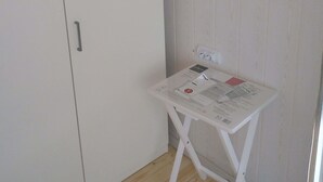 A room with a white wardrobe, a small white table with papers, and a wooden floor.