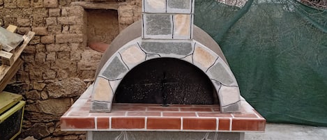A stone-built outdoor pizza oven with a brick base and a stone arch on top.