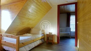 Una stanza con soffitto spiovente, un letto di legno, un comodino e una culla nella stanza adiacente.