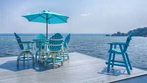 A wooden deck with a table and chairs, an umbrella, and a view of a lake. - Seneca Memories: Luxury Lakeside Home on Seneca Lake! (Penn Yan)
