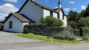 A white house with a stone wall, a chimney, and a small window. - Swallows House - Four Bedroom House, Sleeps 8 (Skelwith)