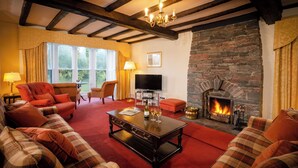 A cozy living room with a stone fireplace, comfortable seating, and a television. - Swallows House - Four Bedroom House, Sleeps 8 (Skelwith)