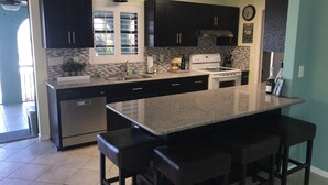 Una cocina moderna con armarios oscuros, una isla grande con taburetes de bar, un lavavajillas de acero inoxidable y un horno empotrado.