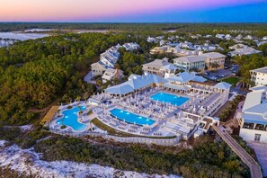 A resort with multiple swimming pools, a large covered area, and a view of the surrounding forest and water.