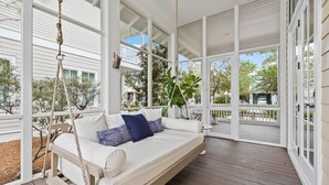 En inglasad veranda med en vit gungstol, ett trädäck och utsikt över det omgivande bostadsområdet.