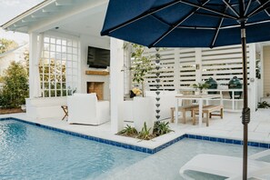 A poolside area with a white outdoor seating area, a grill, and a TV mounted on a wall.