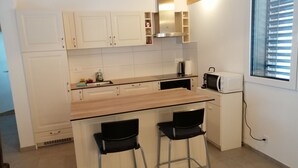 A compact kitchen with a wooden countertop, two bar stools, a microwave, and a window with blinds. - Appartement Individuel (Châtel-Saint-Denis)