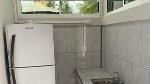 Una cocina compacta con un refrigerador blanco, un lavamanos empotrado y una ventana sobre el lavamanos.
