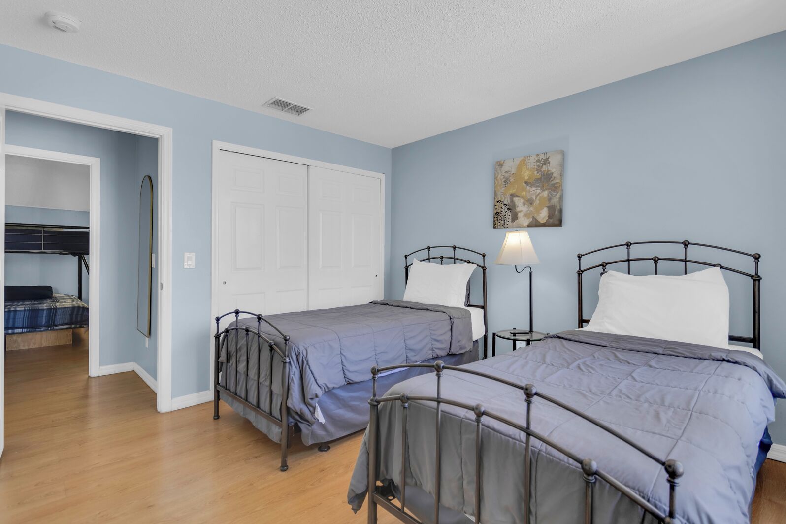 Une chambre avec deux lits en métal, une porte blanche et un tableau accroché au mur.