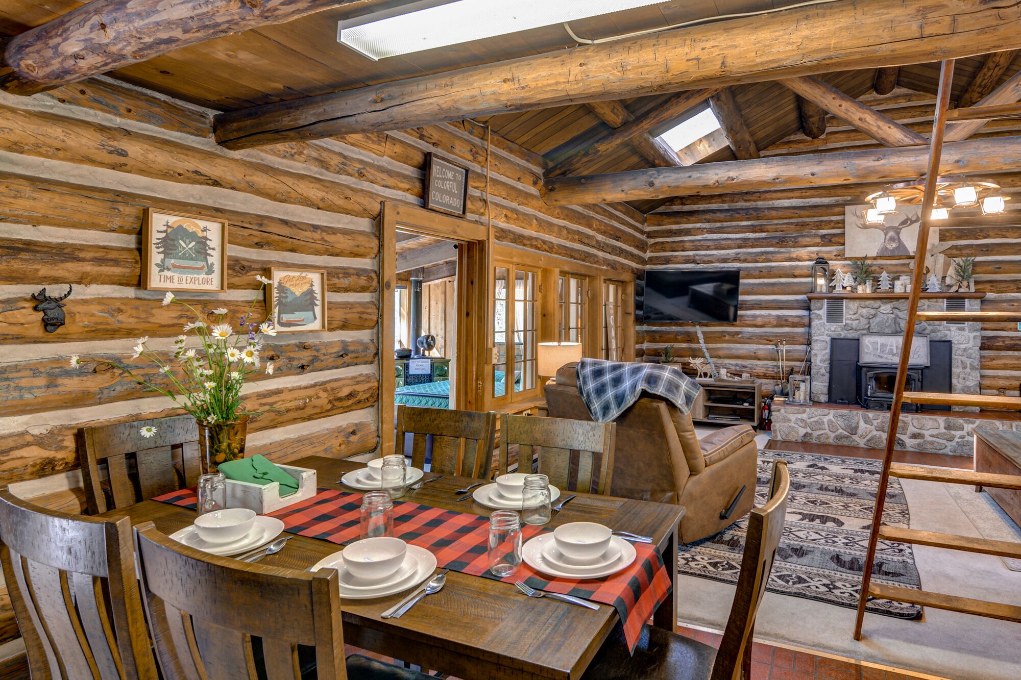L’intérieur d’un chalet rustique en rondins de bois comprend un coin repas, un canapé, une cheminée et un téléviseur.
