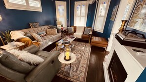 Un salon comprenant un canapé, un fauteuil et un pouf, une table basse avec une bougie et une cheminée.