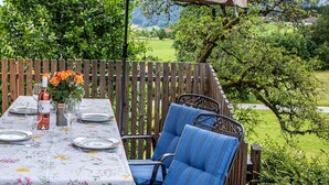 An outdoor dining area with a table set for four, surrounded by blue chairs and a wooden fence. - Ferienwohnung , Terr., Küche, 2 Schlaf- u. 1 Wohn-/schlafz., max 4 P (Ruhpolding)