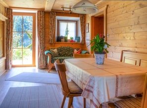 A wooden cabin interior with a dining table, chairs, a sofa, and a potted plant. - Ferienwohnung , Terr., Küche, 2 Schlaf- u. 1 Wohn-/schlafz., max 4 P (Ruhpolding)