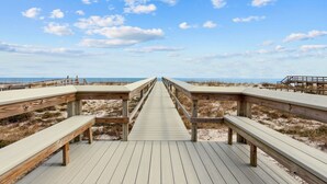 En træpromenade der fører til stranden, med bænke på hver side.