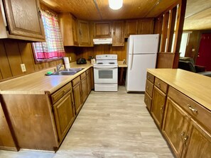 A compact kitchen with wooden cabinets, a white refrigerator, a stove, and a sink. - Walk 2 River & Entertainment & Hippie Chicks, River Road, Heart of Concan! (Concan)