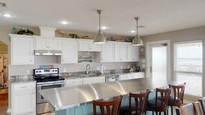 Uma cozinha moderna com armários brancos, eletrodomésticos de aço inoxidável, iluminação pendente e uma ilha central com banquetas.