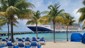 A beach with rows of blue and white lounge chairs, palm trees, and a large cruise ship docked at a pier. - Oceanfront Resort-Style Home3br, 2Ba - Private Pool & Island car included (Cockburn Town)