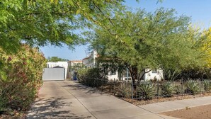 A paved pathway flanked by greenery and a metal fence, leading to a building with a white facade and a red-tiled roof.