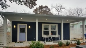 A house with a dark exterior, a white door, and a covered porch with two white chairs and a table. - In Town. Pet Friendly. Quiet Neighborhood. Queen Bed. Perfect Getaway! (Fredericksburg)
