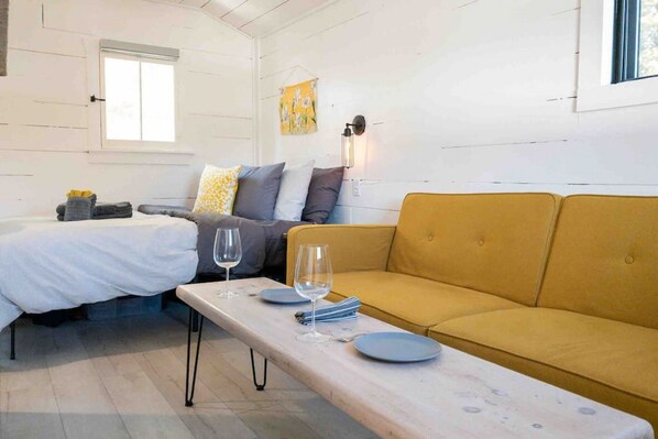 Una habitación con cama, sofá, una mesa con platos y vasos, y una ventana.