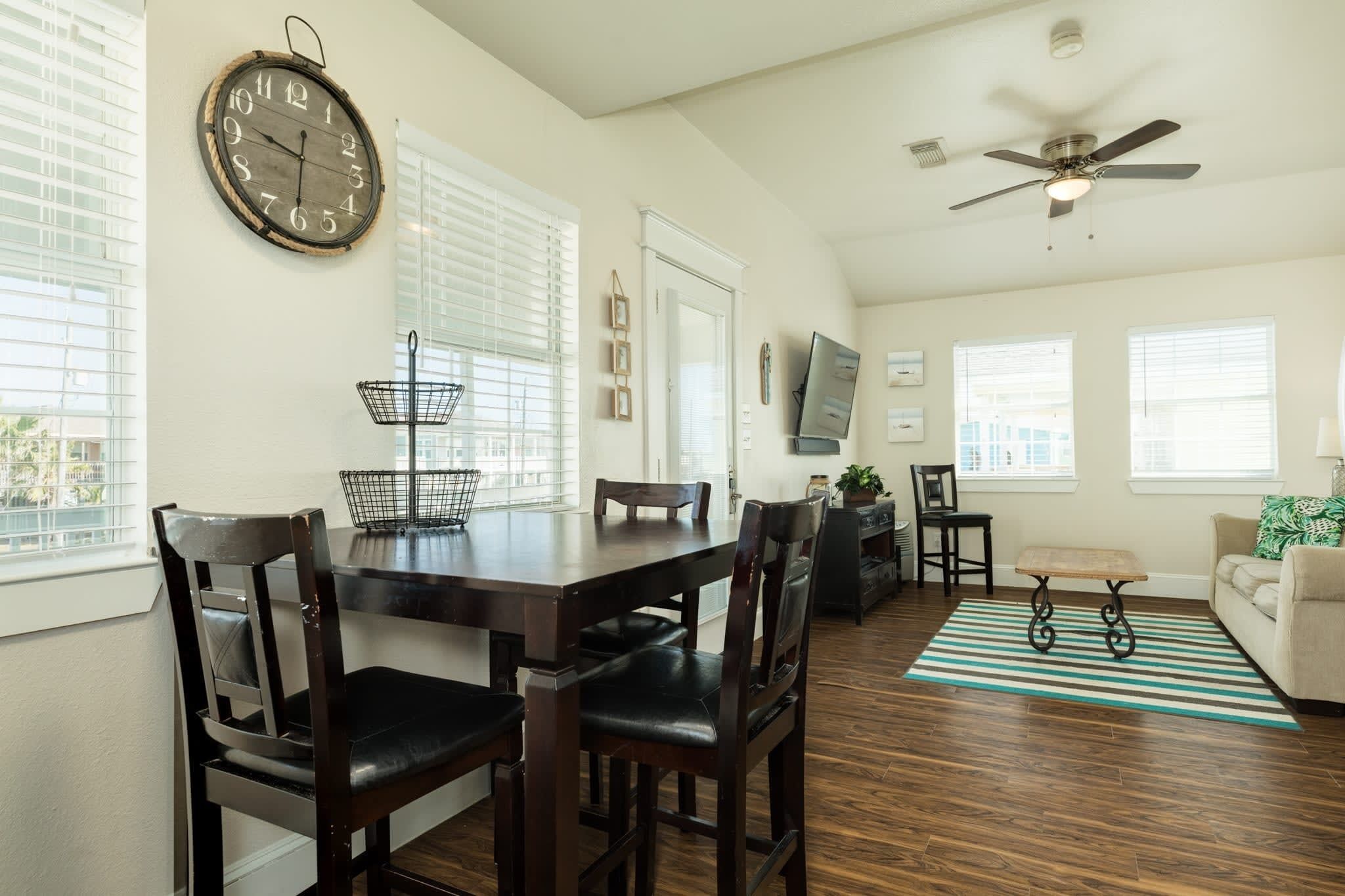 A dining area with a wooden table, chairs, a clock, and a TV.