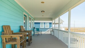 Eine überdachte Veranda mit Holzbanken und Stühlen, einem Geländer und Blick auf den Strand.