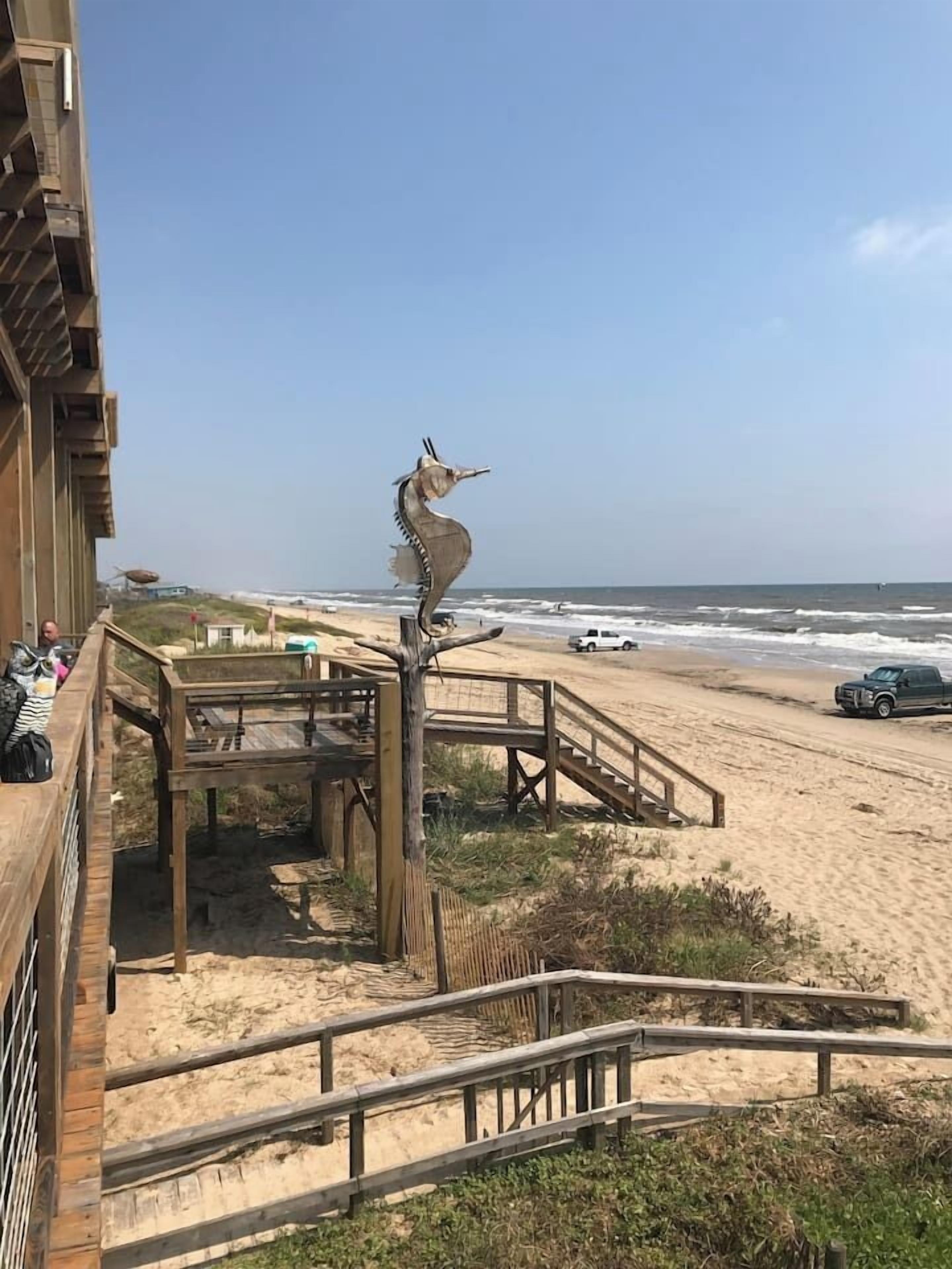 Una escalera de madera que lleva a una zona de playa con una escultura de caballito de mar.