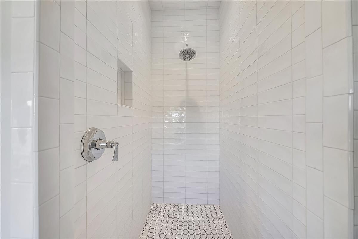 Une douche étroite, carrelée, avec une seule pomme de douche et un robinet fixé au mur.