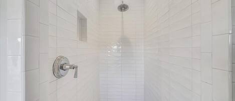 Une douche étroite, carrelée, avec une seule pomme de douche et un robinet fixé au mur.