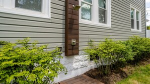 A house with a gray siding exterior, a wooden mailbox, and green shrubs.