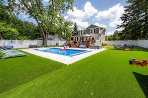 Un jardin avec une piscine, une terrasse et une pelouse.