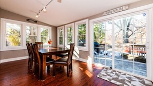 A dining area with a wooden table and chairs, large windows, and a view of the backyard.