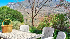 A patio with a table and chairs, a wicker basket, and a view of mountains and greenery.