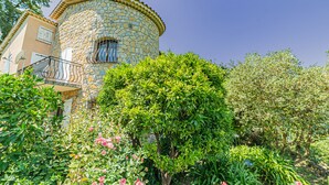 A stone building with a balcony, surrounded by lush greenery and flowering plants.