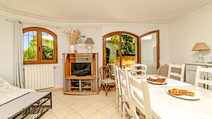A compact living space with a sofa, dining table, chairs, a TV, and a window with a view of greenery.