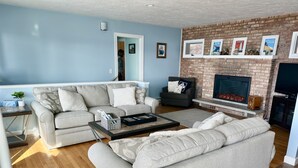 Ein Wohnzimmer mit einer Sofagarnitur, einem Couchtisch, einem Kamin und einer Ziegelwand mit gerahmten Bildern.
