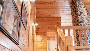 A wooden staircase with handrails, framed pictures on the wall, and a stone wall on the right. - On Beautiful White River, Minutes from Sylamore Creek and Blanchard Springs (Mountain View)