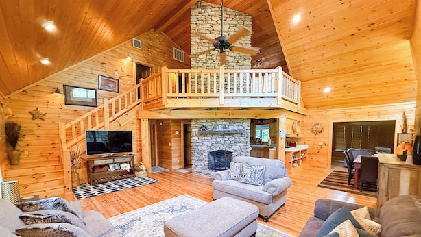 A spacious log cabin interior with a stone fireplace, a balcony, a dining area, and a television in the living room. - On Beautiful White River, Minutes from Sylamore Creek and Blanchard Springs (Mountain View)