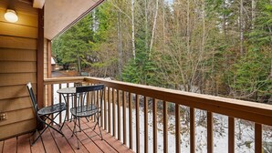 A wooden deck with a railing, two chairs, and a table.