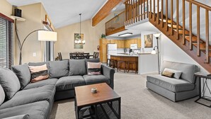 A spacious living area with a gray sectional sofa, a wooden coffee table, and a staircase leading to an upper level.