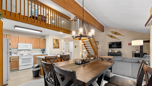 A spacious kitchen with wooden cabinets, a dining area with a wooden table and chairs, a staircase leading to an upper level, and a living area with a sofa and a television.