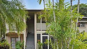 A two-story building with a balcony, a staircase, and surrounding greenery.