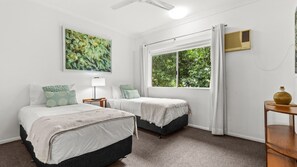 A room with two beds, a window with curtains, a ceiling fan, and a wall-mounted air conditioner.