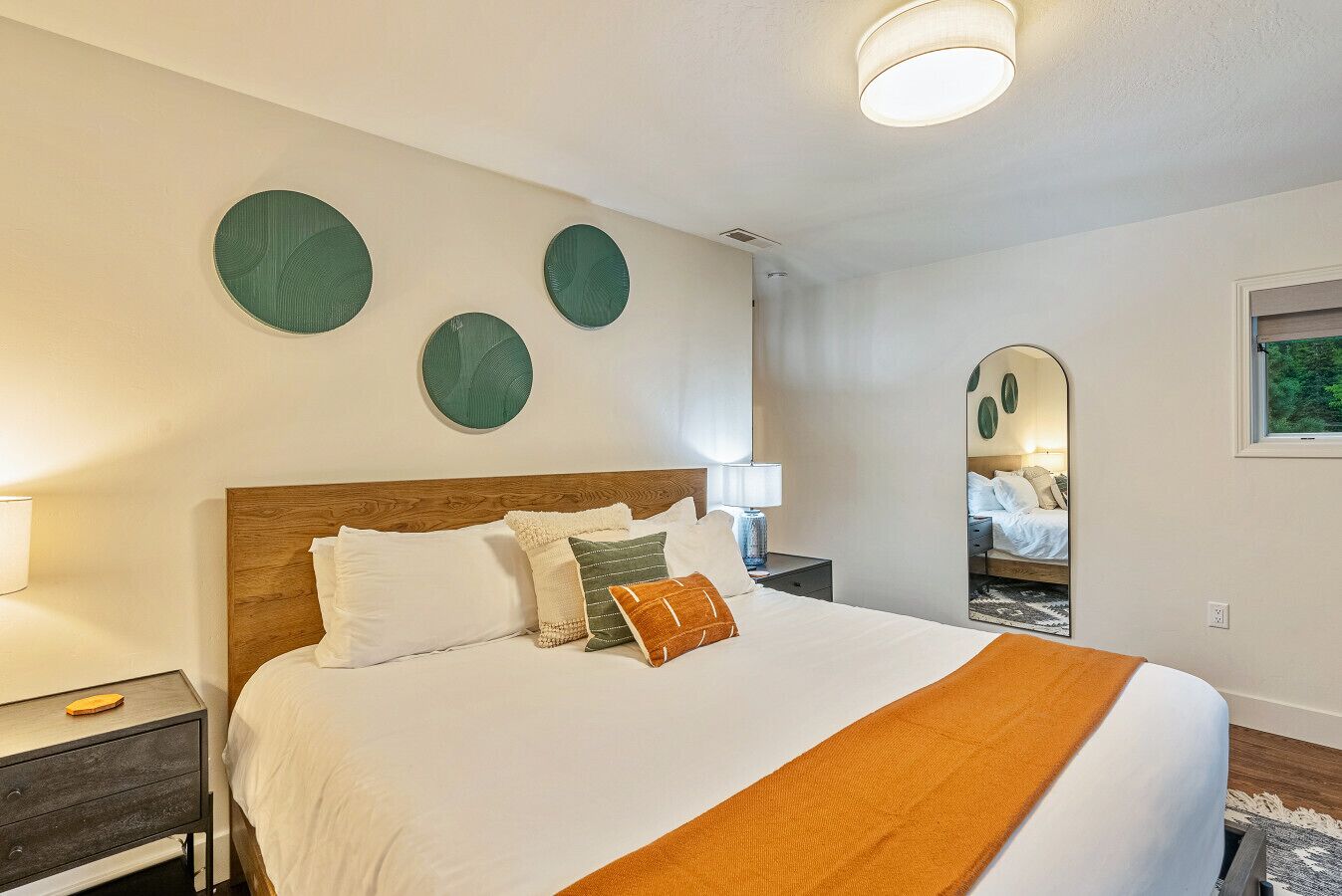 A neatly arranged bedroom with a large bed, a nightstand, a mirror, and three wall-mounted circular decorations.